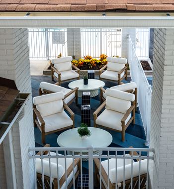 A patio with white chairs and a table with a plant on it.